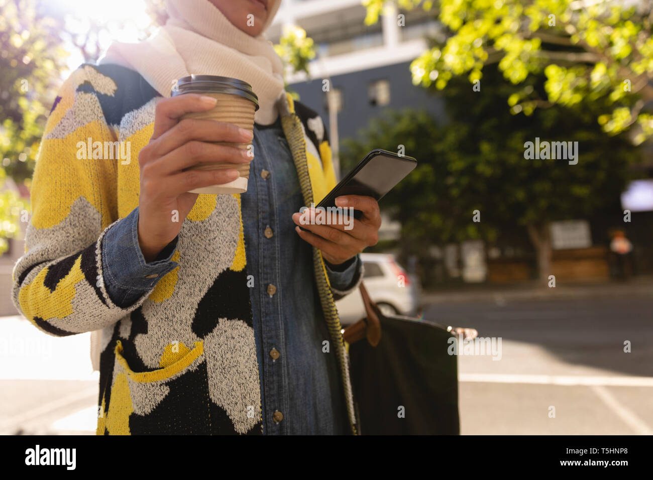 Donna che utilizza il cellulare mentre un caffè in strada in una giornata di sole Foto Stock