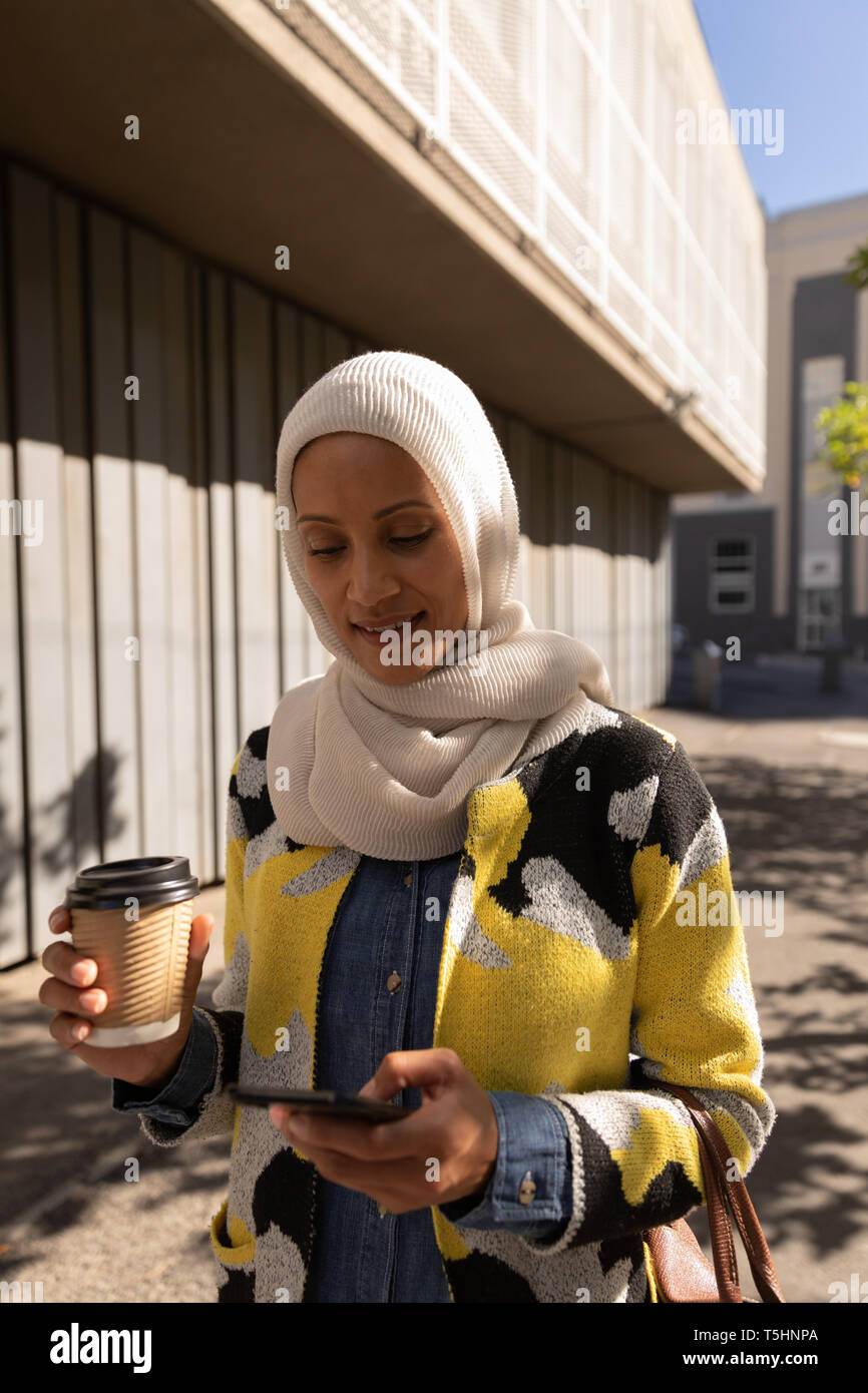 Donna che utilizza il cellulare mentre un caffè in strada in una giornata di sole Foto Stock