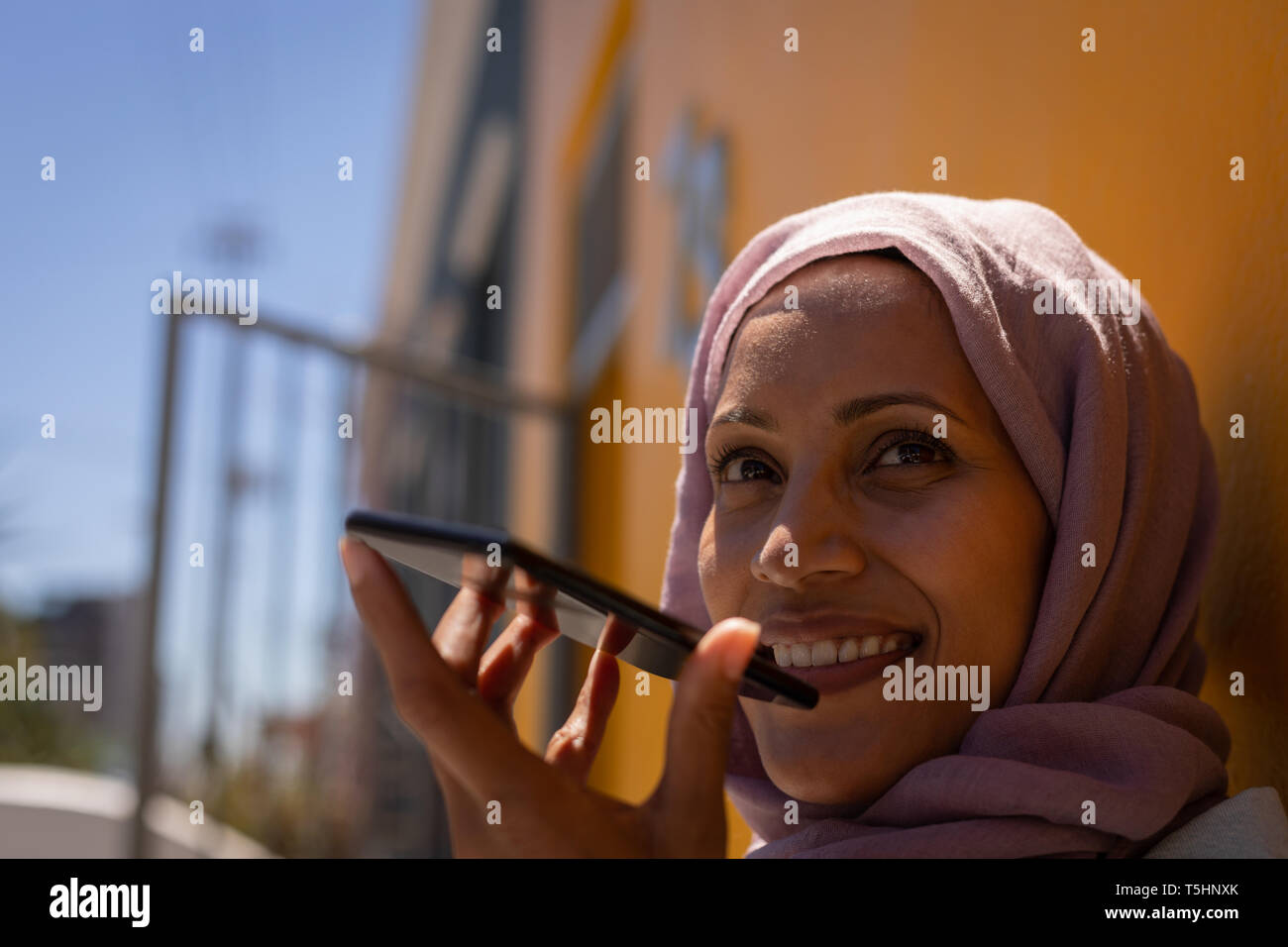 Donna che parla al cellulare mentre appoggiata al muro in una giornata di sole Foto Stock