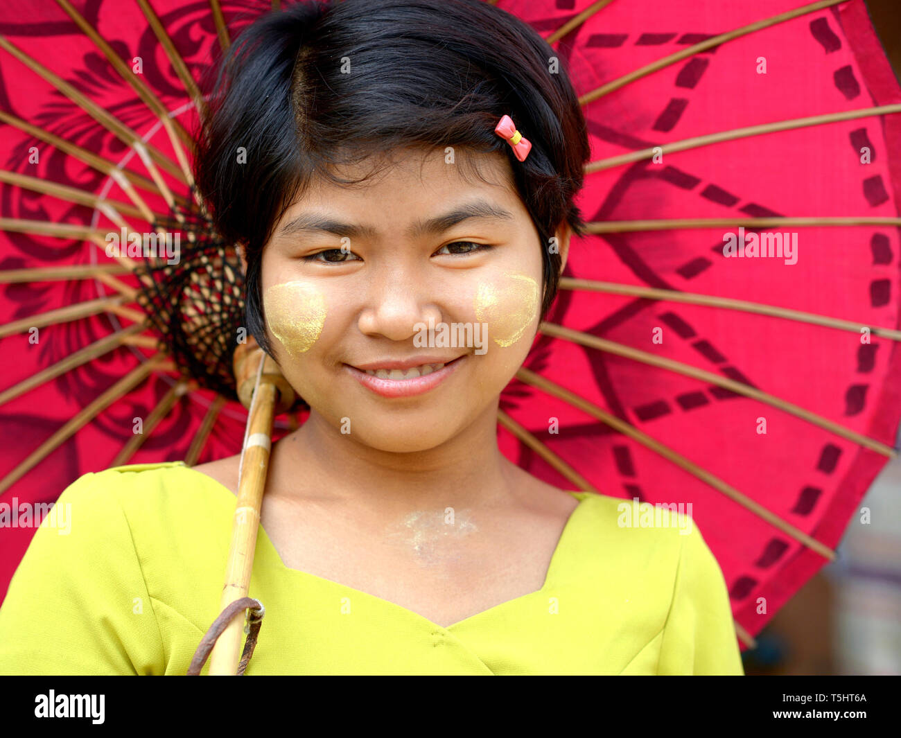 Ragazza birmano con thanaka cosmetica viso sulle sue guancie pone per la fotocamera in un tradizionale birmana ombrellino di carta. Foto Stock