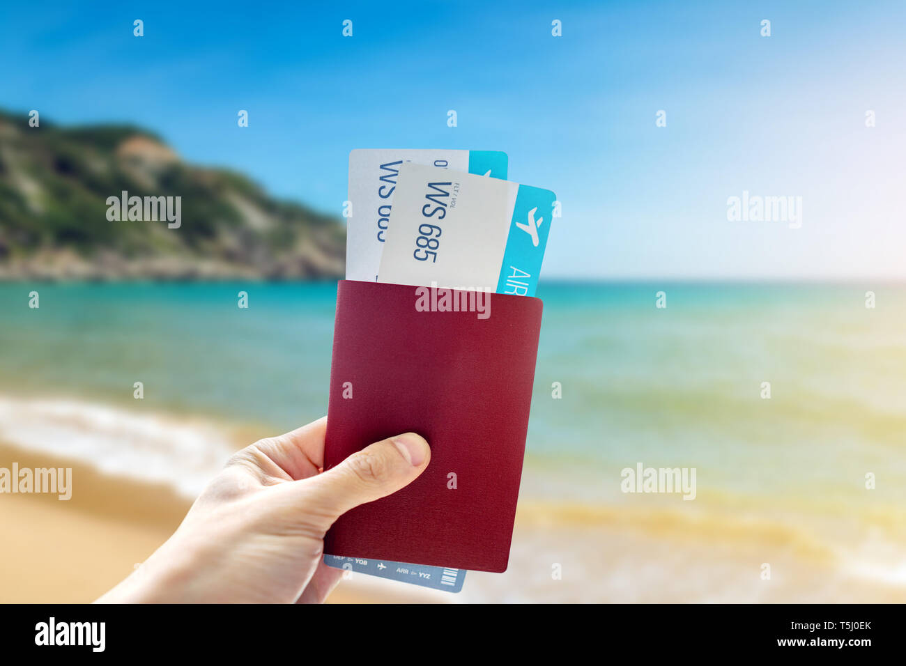 La mano in possesso di un passaporto in corso di validità e due biglietti aerei su uno sfondo blu del mare. Il concetto di viaggi e vacanze in splendidi luoghi esotici Foto Stock