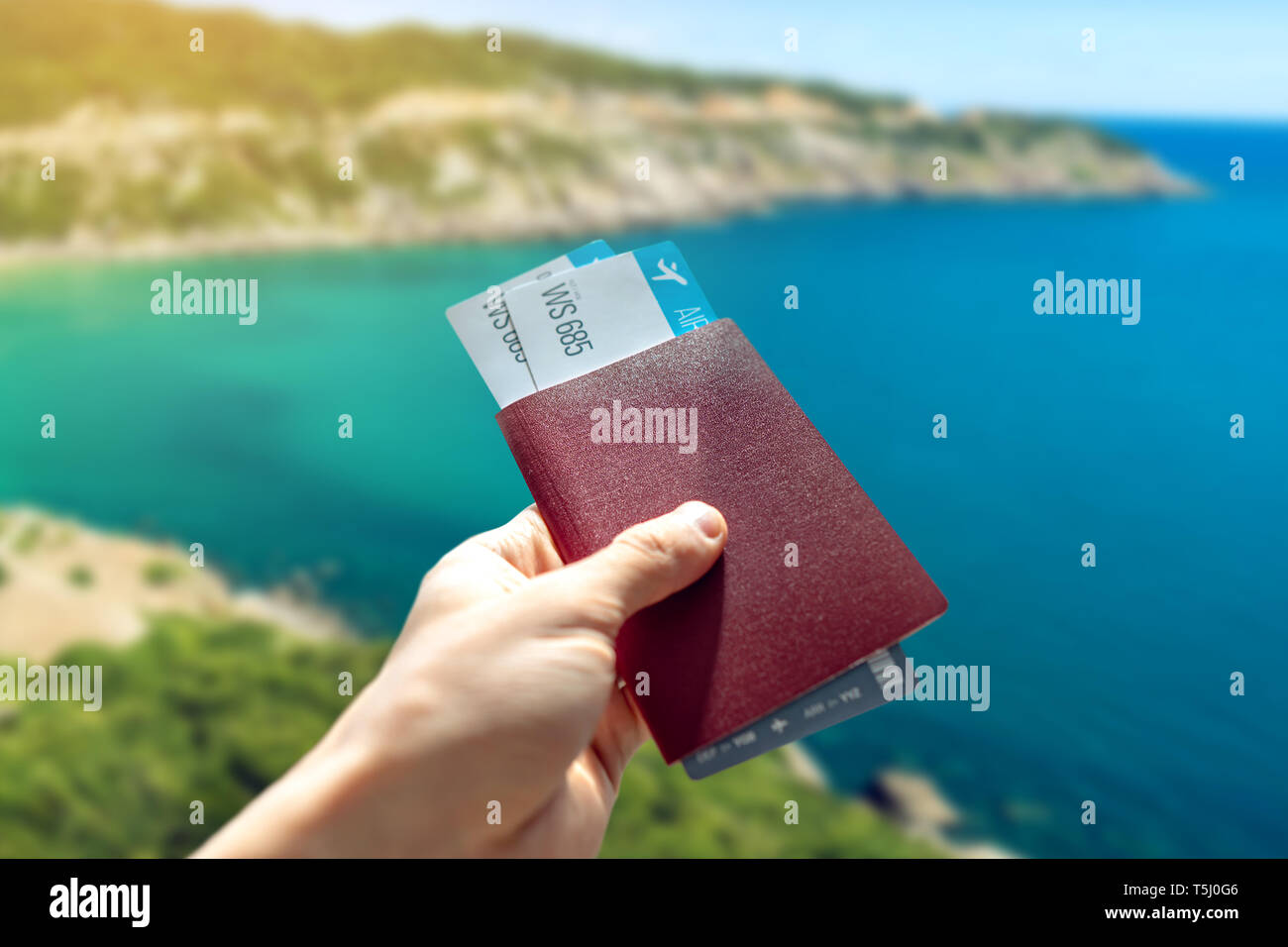 La mano in possesso di un passaporto in corso di validità e due biglietti aerei su uno sfondo blu del mare. Il concetto di viaggi e vacanze in splendidi luoghi esotici Foto Stock