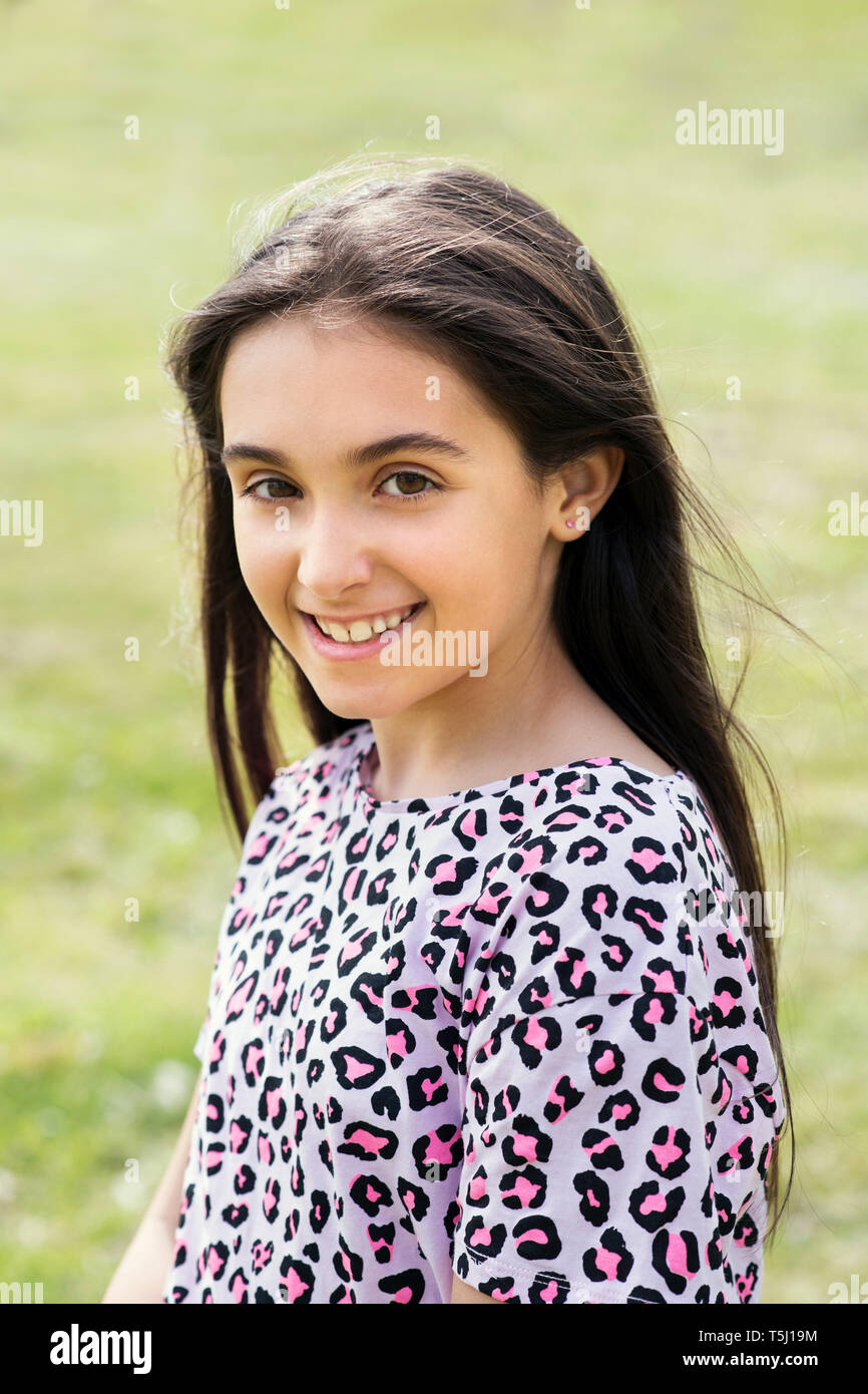 Sorridente ragazza giovane e carina con lunghi capelli scuri che indossa una rosa e nero animale maculato print top all'aperto in giardino Foto Stock
