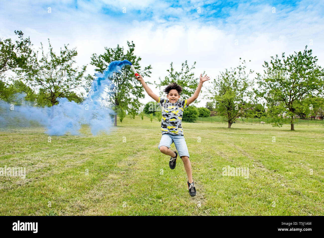 Felice di spensierata giovane ragazzo giocando con una svasatura blu in tutta l'erba fumo posteriore dietro di lui un fresco verde parco o giardino Foto Stock