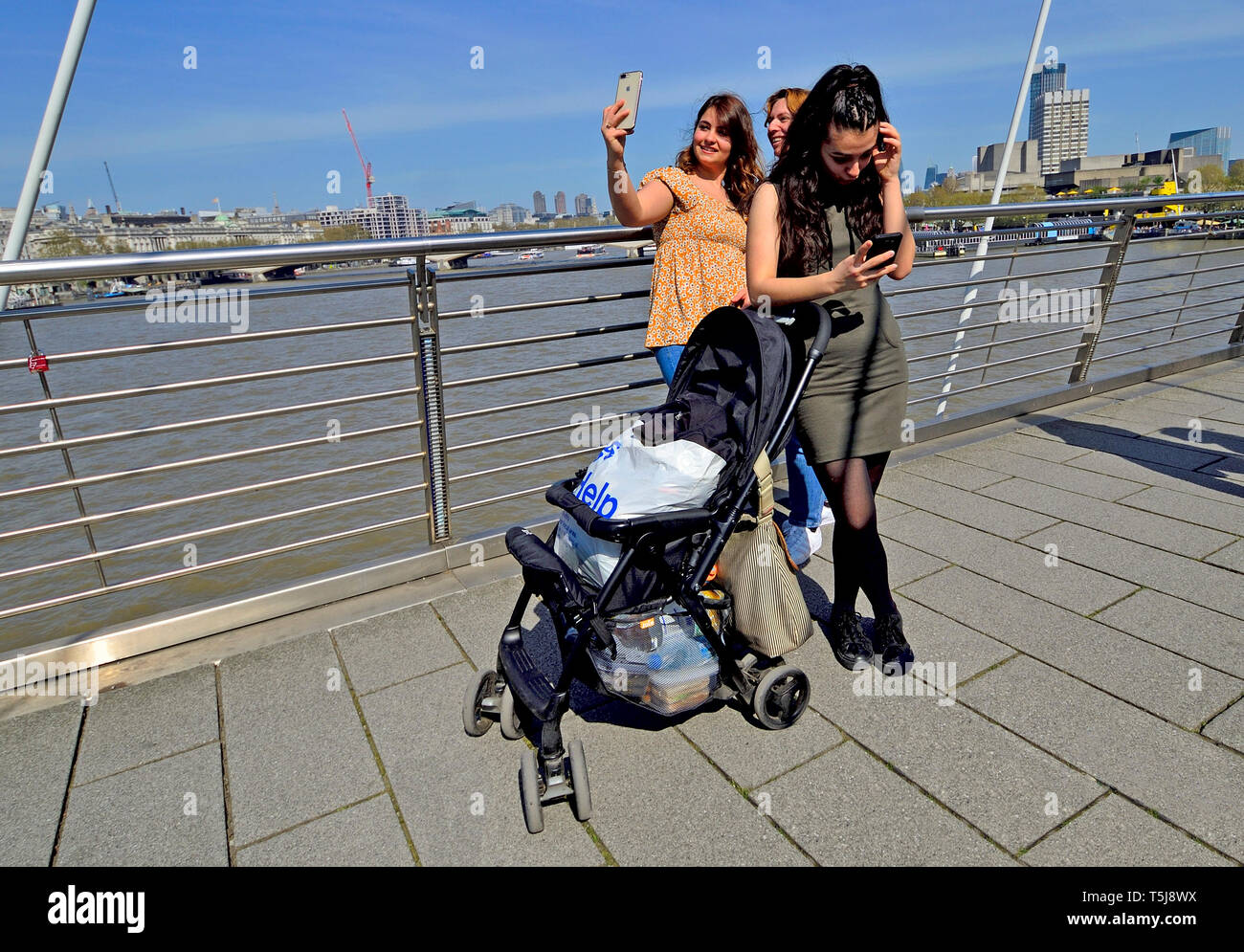 Londra, Inghilterra, Regno Unito. Giovani donne sul Millennium Bridge con i loro telefoni cellulari, prendendo un selfie Foto Stock
