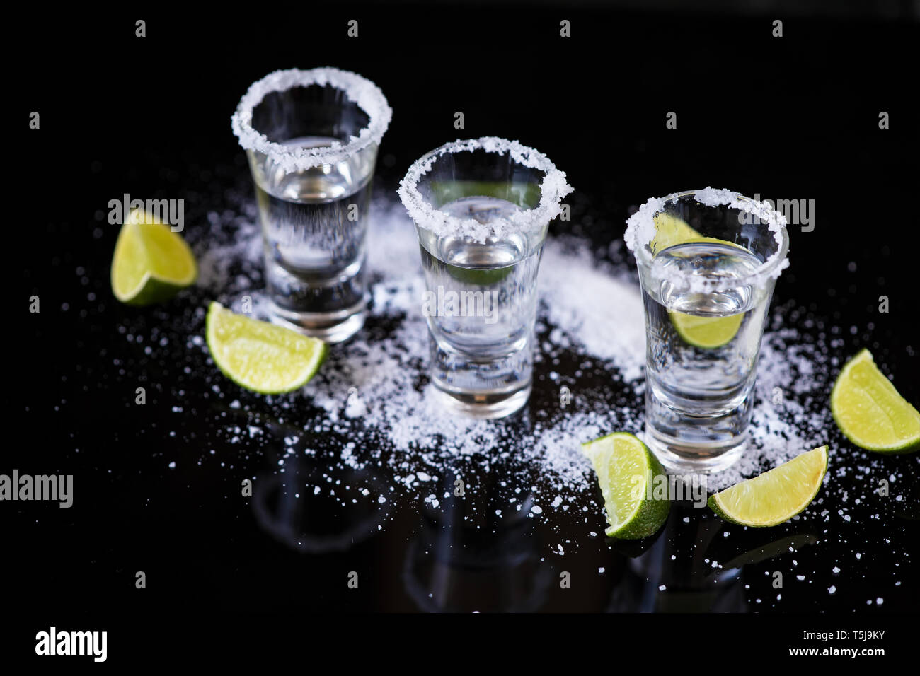 Tre colpi di Tequila con calce e sale su sfondo nero Foto Stock