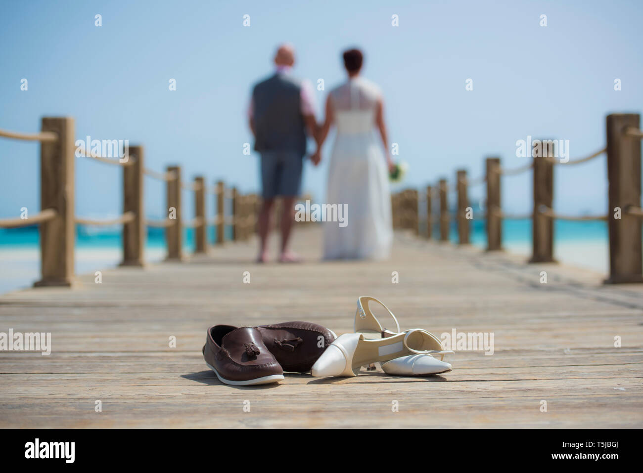 Coppia sposata sul giorno di nozze camminando romanticamente esterno sul molo in legno con un paio di scarpe in primo piano Foto Stock