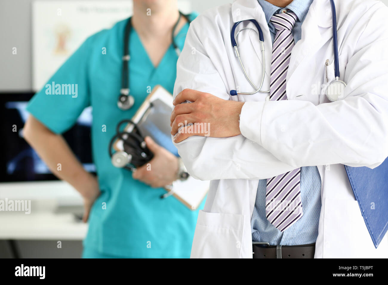 Medico maschio con le braccia incrociate sul petto in piedi in linea con i colleghi in ufficio Foto Stock