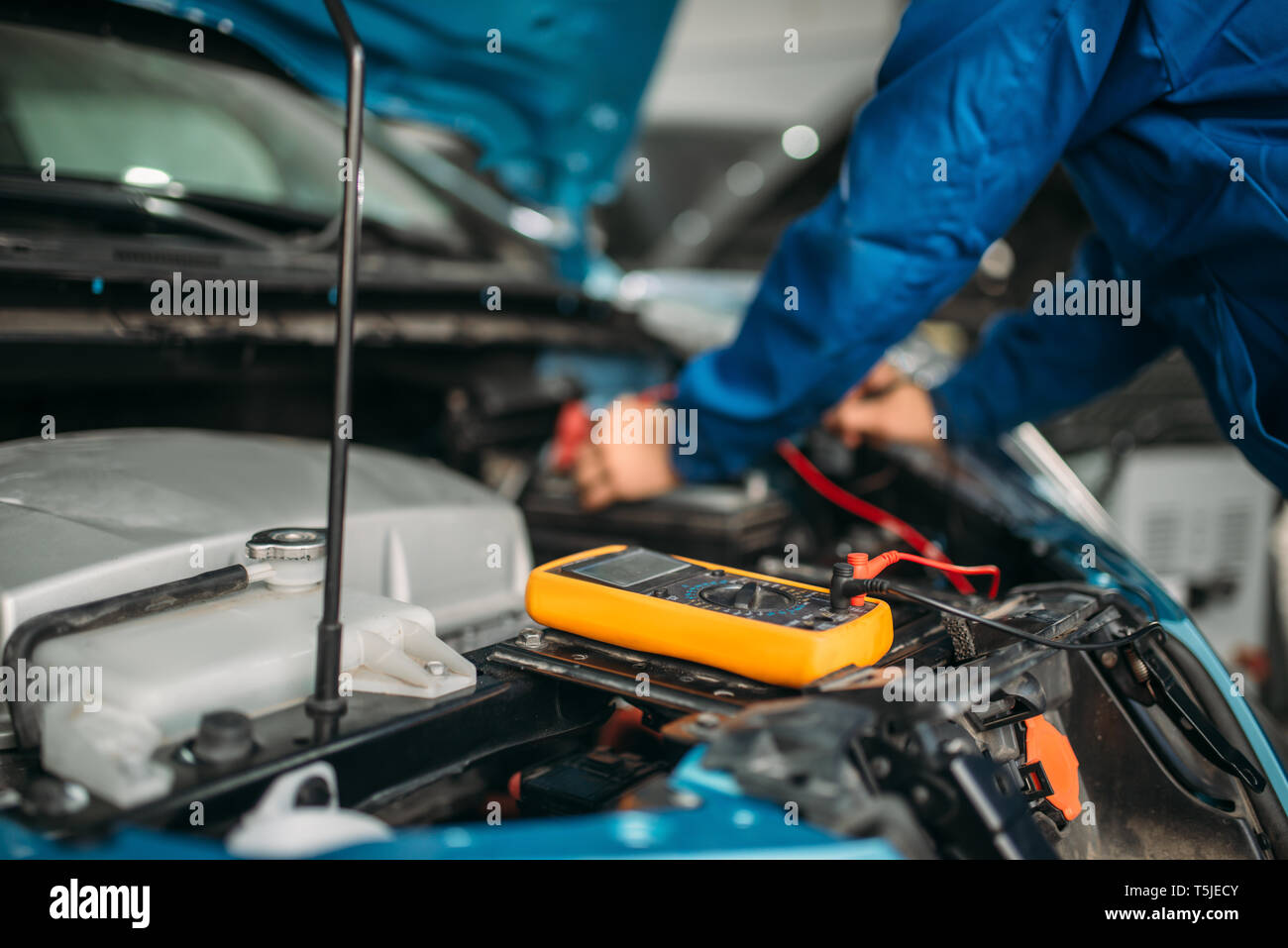 Elettrauto con multimetro controlla il livello di carica della batteria. Auto-service, veicolo diagnosi del cablaggio Foto Stock