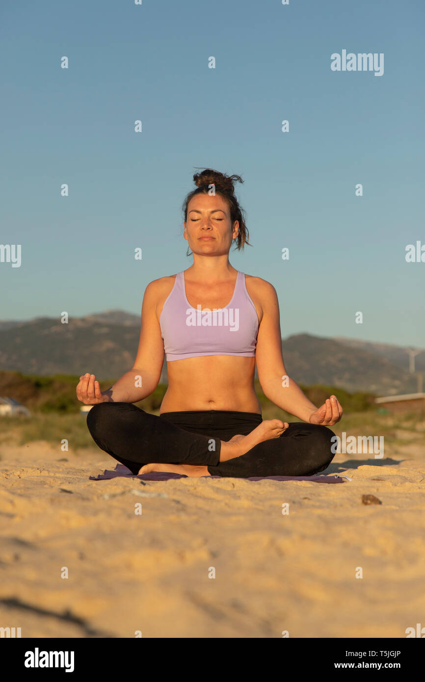 Donna meditando sulla spiaggia la sera Foto Stock