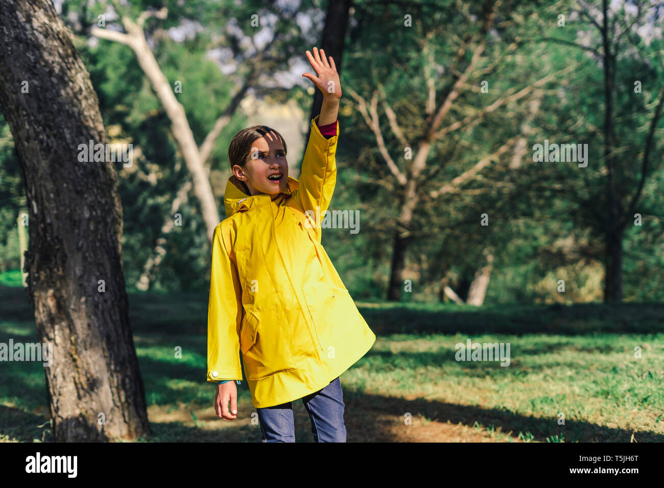 Ragazza che indossa un impermeabile giallo permanente al sole schermare gli occhi con la mano Foto Stock