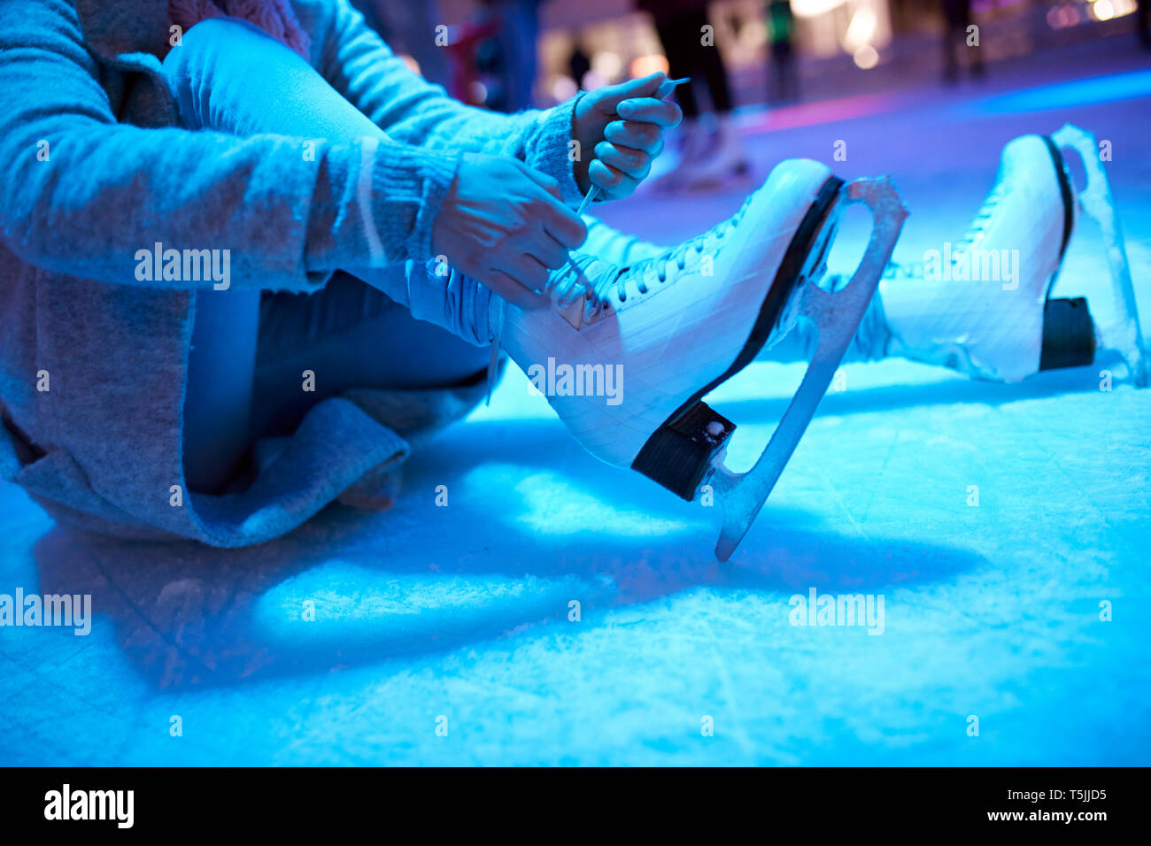 Donna seduta sulla pista di pattinaggio su ghiaccio a mettere su pattini da ghiaccio Foto Stock