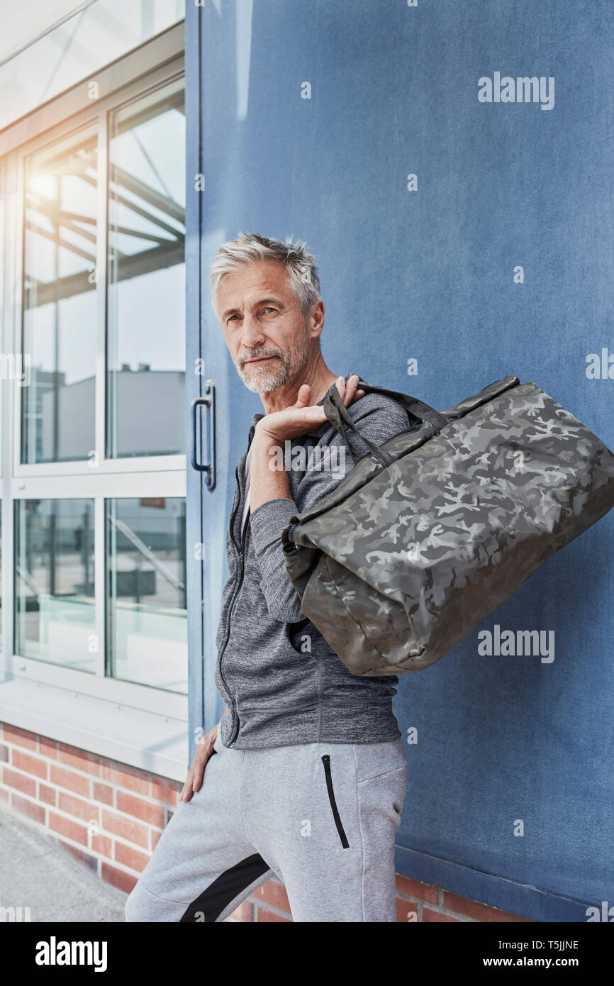 Ritratto di uomo maturo con camouflage borsa sportiva in piedi nella parte anteriore della palestra Foto Stock