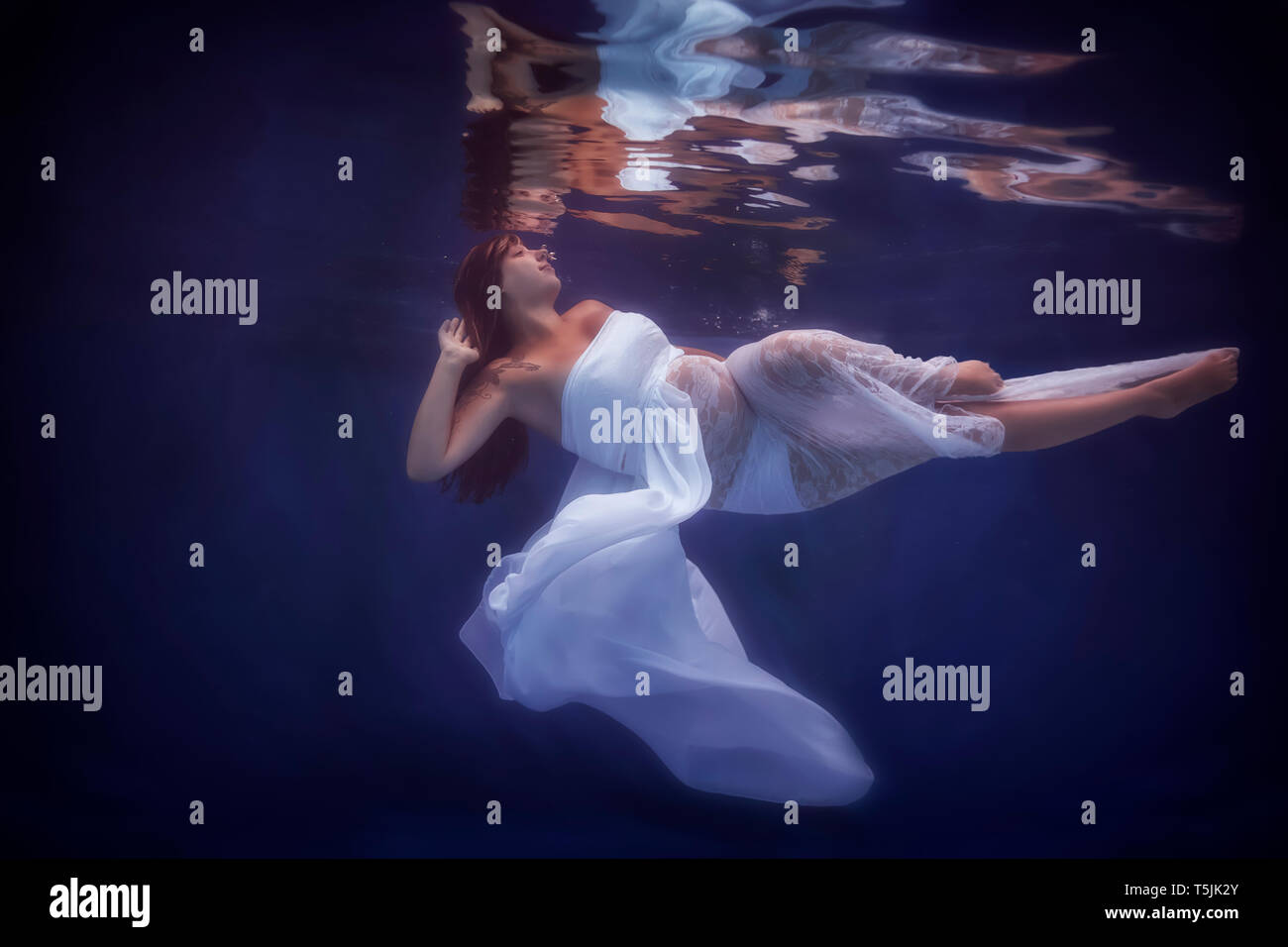 Donna incinta indossando abito bianco sotto l'acqua Foto Stock
