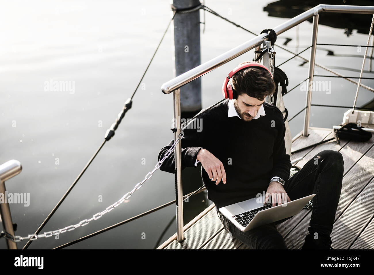 Imprenditore in houseboat utilizzando laptop, indossando le cuffie Foto Stock