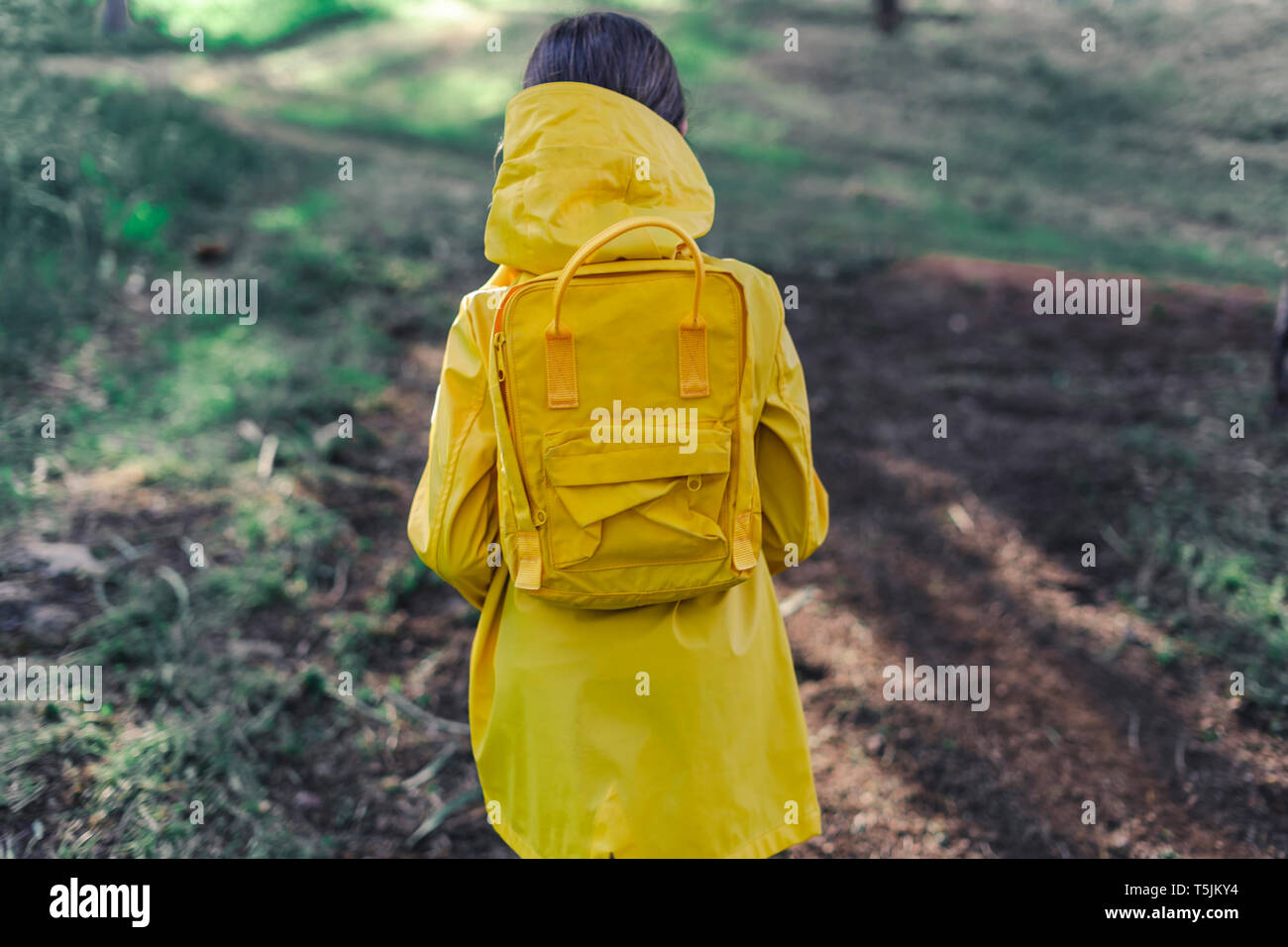 Vista posteriore di una ragazza che indossa un impermeabile giallo e giallo zaino in natura Foto Stock