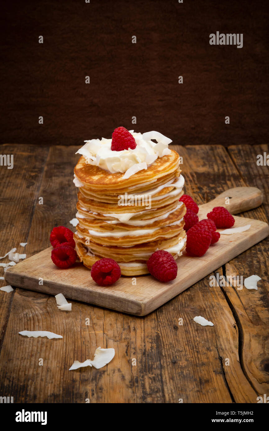 Frittelle di farina di mandorle con lamponi, yogurt greco e scaglie di noce di cocco sul pannello di legno Foto Stock