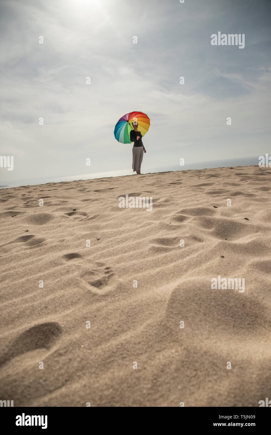 Donna con ombrello coloratissimo in piedi presso la spiaggia Foto Stock