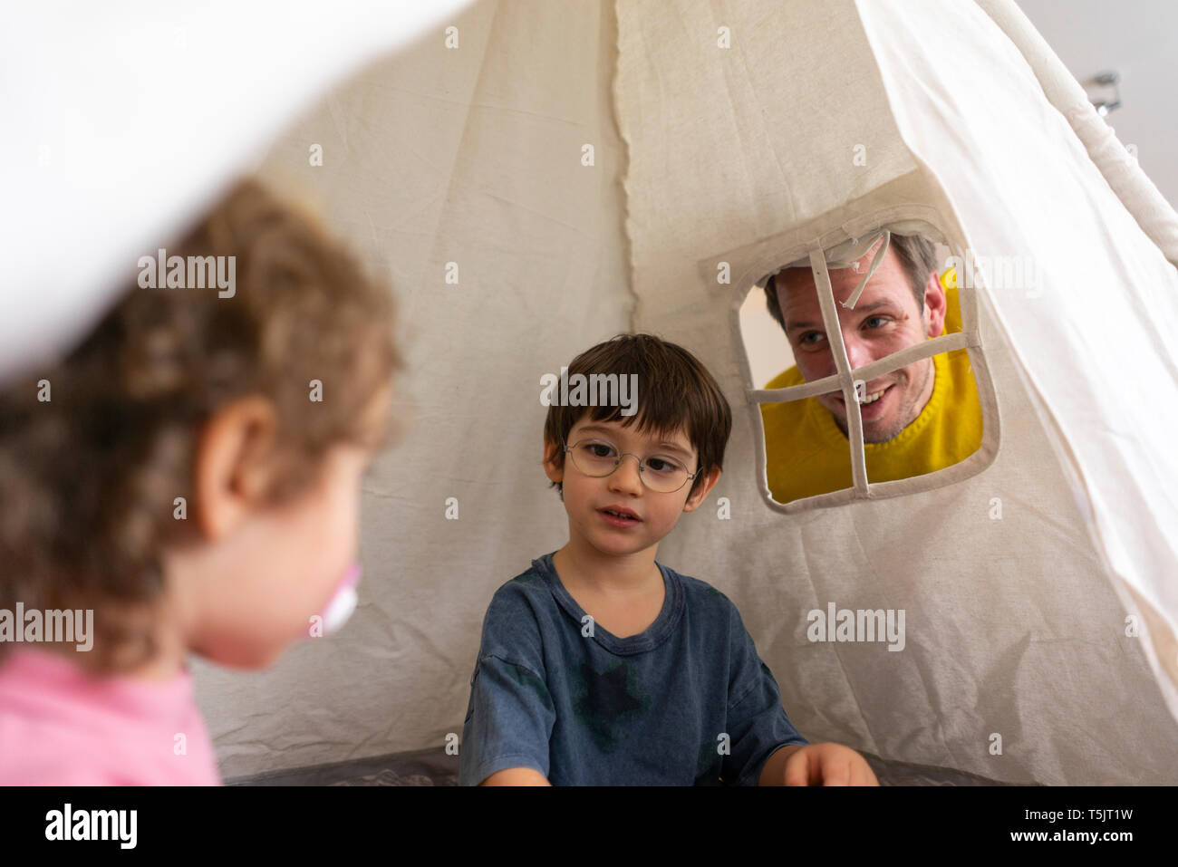 Padre guardando choldren giocando in un gioco tenda Foto Stock
