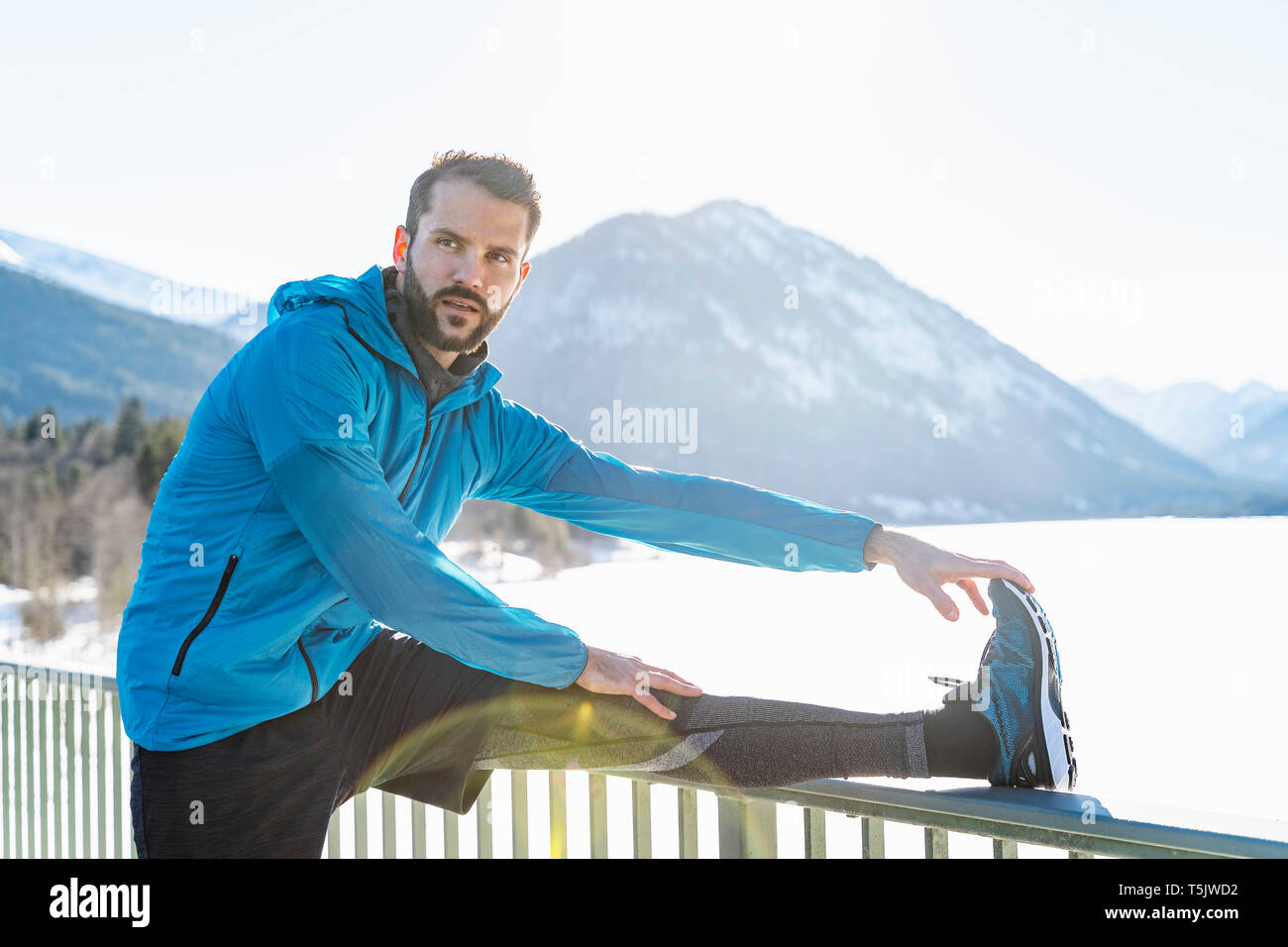 In Germania, in Baviera, sportive uomo allungamento in inverno sulla ringhiera del ponte Foto Stock