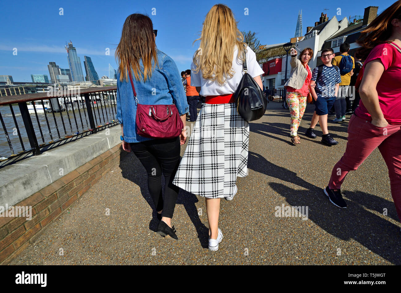 Londra, Inghilterra, Regno Unito. Due giovani donne camminando sulla South Bank, la città di Londra in background (sinistra) Foto Stock