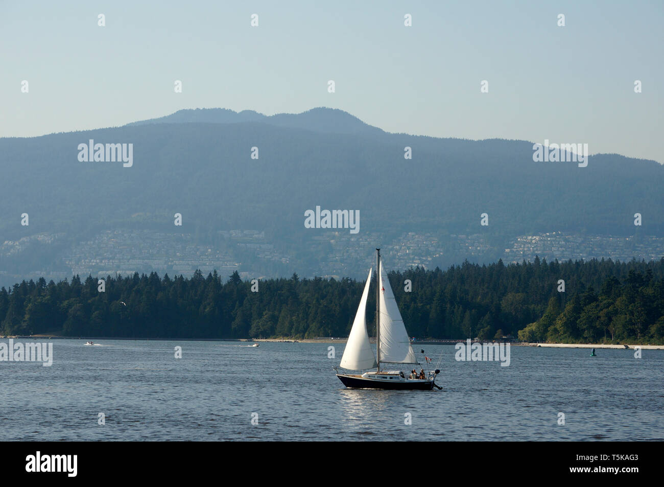 Barca a vela su English Bay con Stanley Park e North Shore Mountains sullo sfondo, Vancouver, BC, Canada Foto Stock