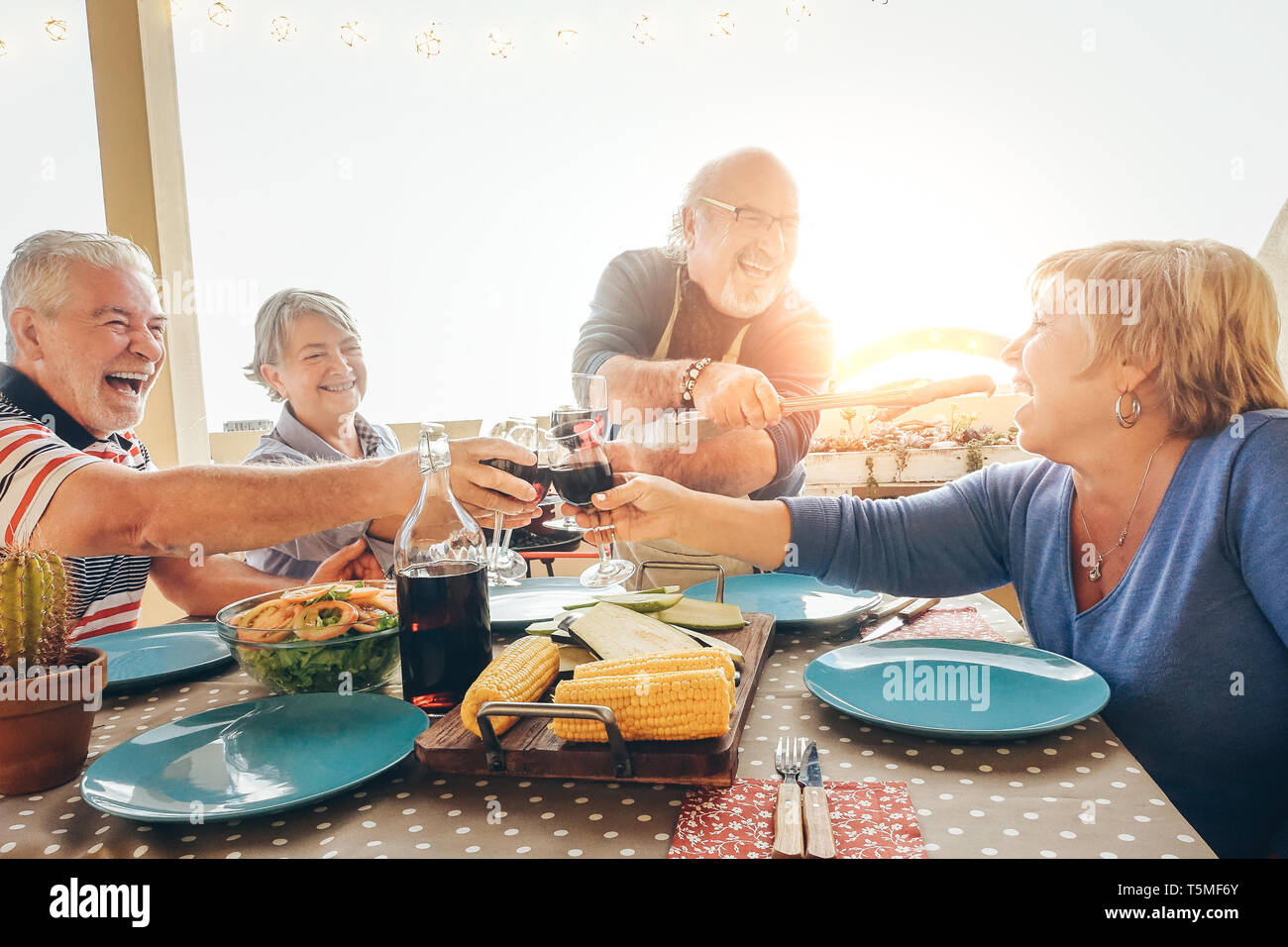 Felice senior amici divertendosi tifo con un bicchiere di vino rosso al barbecue in terrazza outdoor - anziani pasti a base di carne alla griglia e ridere insieme Foto Stock