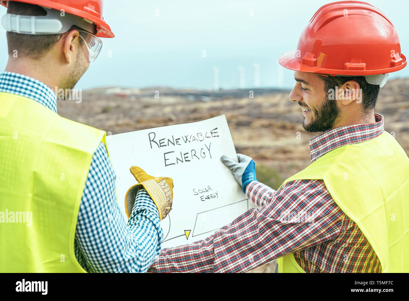 Gli ingegneri di lavoratori di lettura e di parlare del nuovo progetto di energia rinnovabile - due costruttori di discutere le modalità per costruire il mulino a vento e pannelli solari Foto Stock Gli ingegneri di lavoratori di lettura e di parlare del nuovo progetto di energia rinnovabile - due costruttori di discutere le modalità per costruire il mulino a vento e pannelli solari Foto Stock