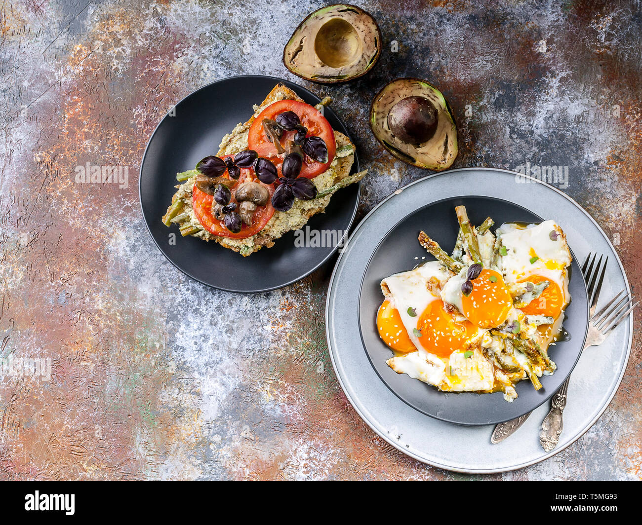 Uova fritte con asparagi, sandwich con pesto, pomodori e funghi, avocado maturo. Una gustosa prima colazione. Vista superiore Foto Stock