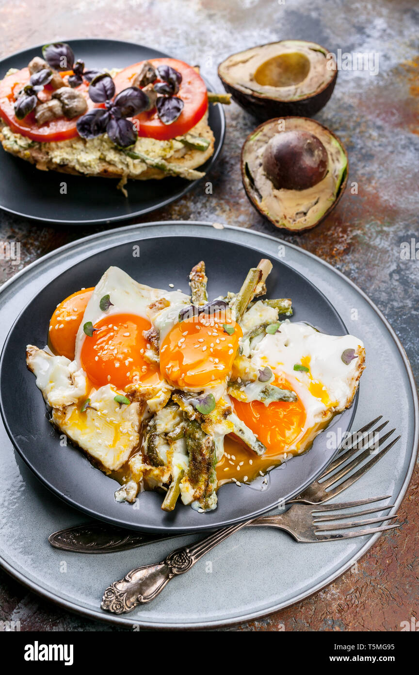 Uova fritte con asparagi, sandwich con pesto, pomodori e funghi, avocado maturo. Una gustosa prima colazione. Foto Stock