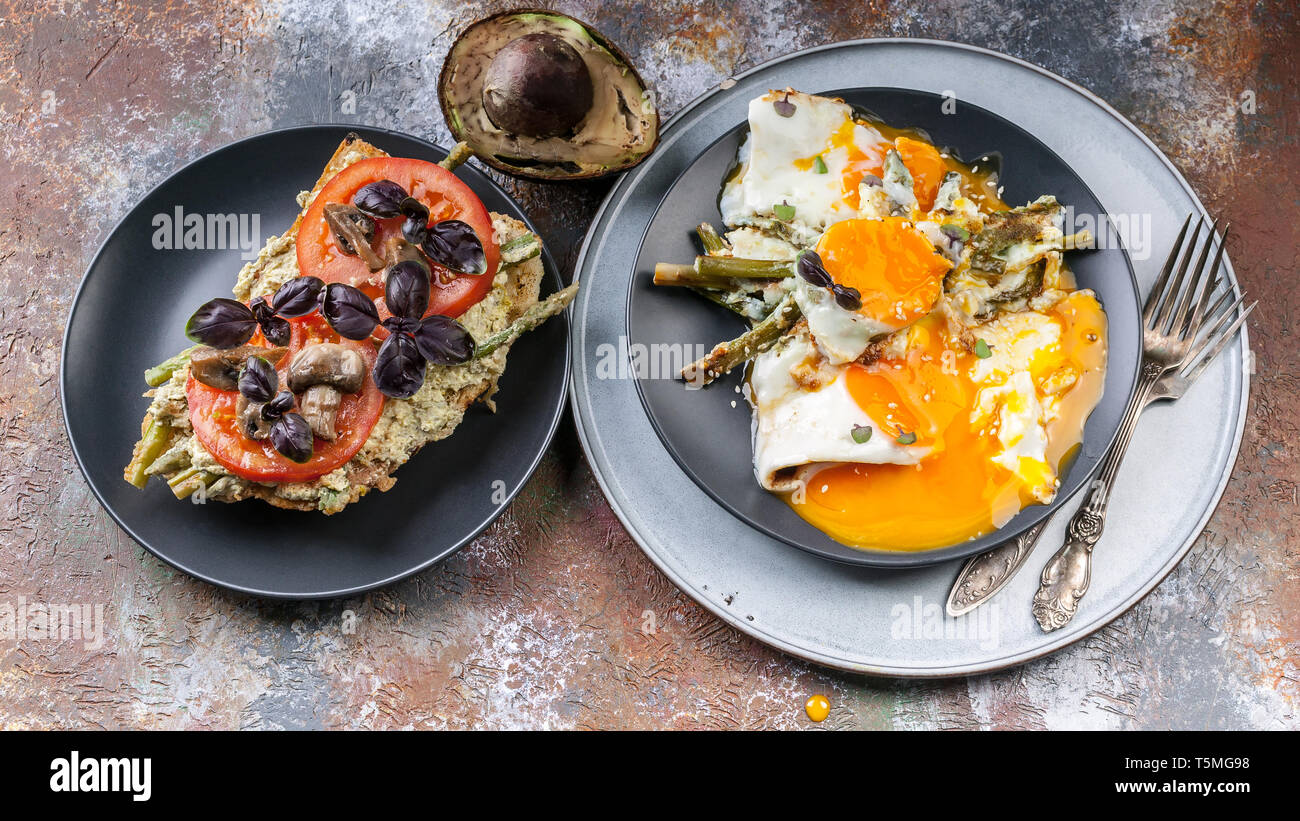 Una gustosa prima colazione. Sandwich con pomodori e funghi, basilico, avocado, uova fritte con asparagi. Vista superiore Foto Stock