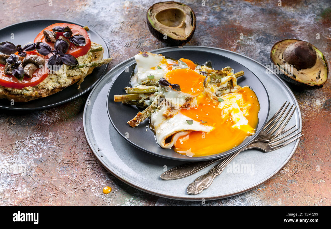 Una gustosa prima colazione. Sandwich con pomodori e funghi, avocado, uova fritte con asparagi. Foto Stock