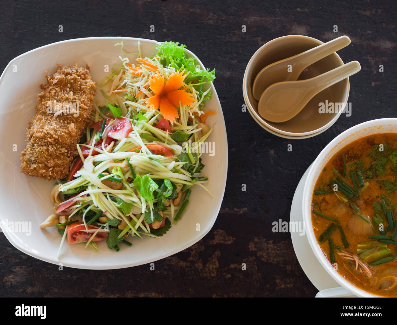 Amaro e piccante Tom Yum Goong minestra e insalata verde con mango e pesce impanati su piastra su un tavolo in un ristorante. Thai autentica cucina tradizionale. a Foto Stock