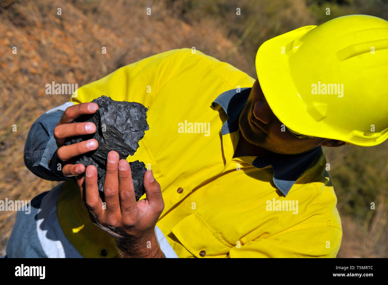 Un minatore di indossare indumenti ad elevata visibilità, tenendo in mano un pezzo di materie del carbone. In corrispondenza di una grande miniera di carbone sito. Foto Stock