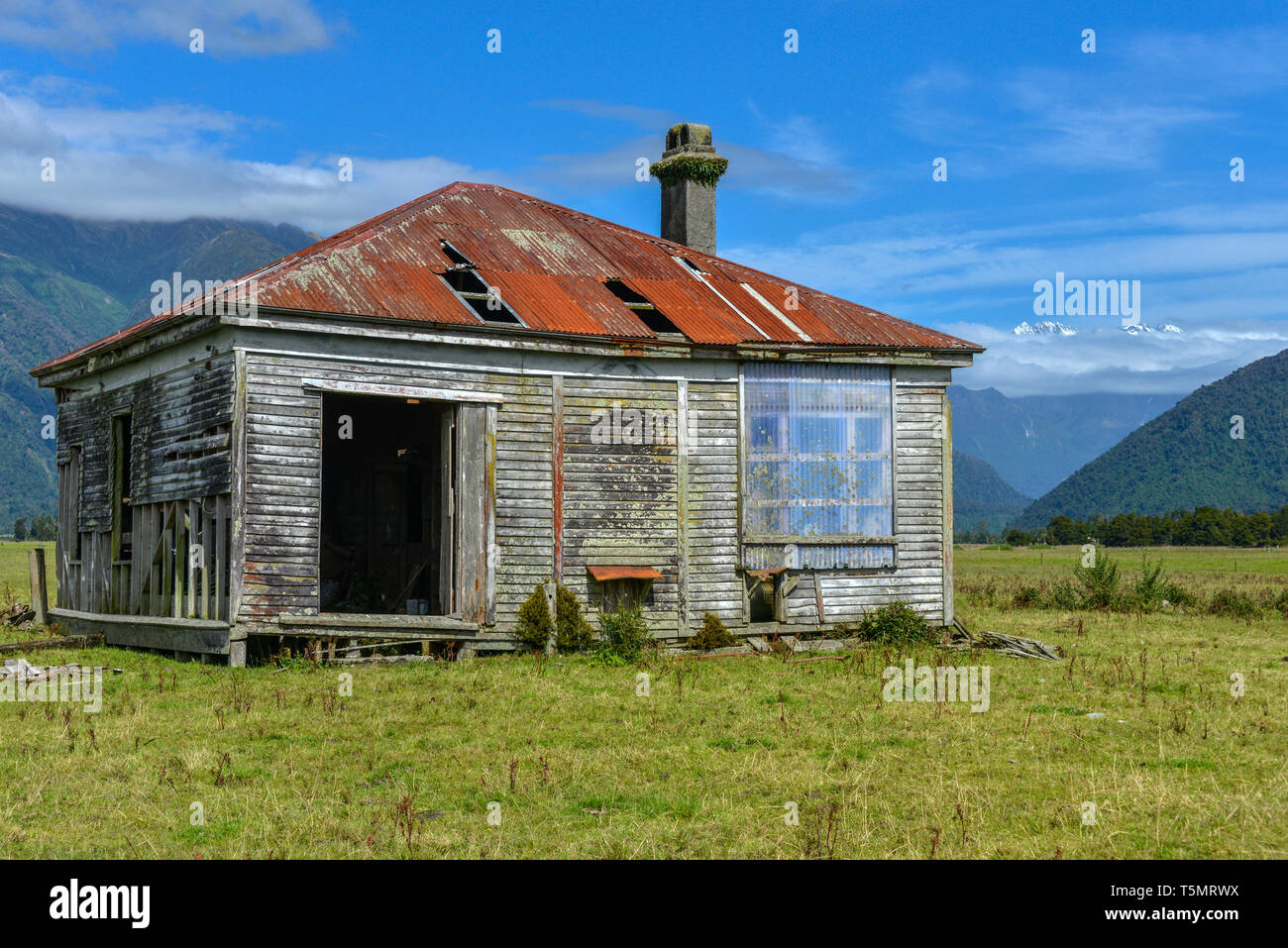 Un abbandonato, casa di legno vicino Whataroa, nell'Isola del Sud della Nuova Zelanda. Le Alpi del Sud la gamma della montagna è visibile in background. Foto Stock