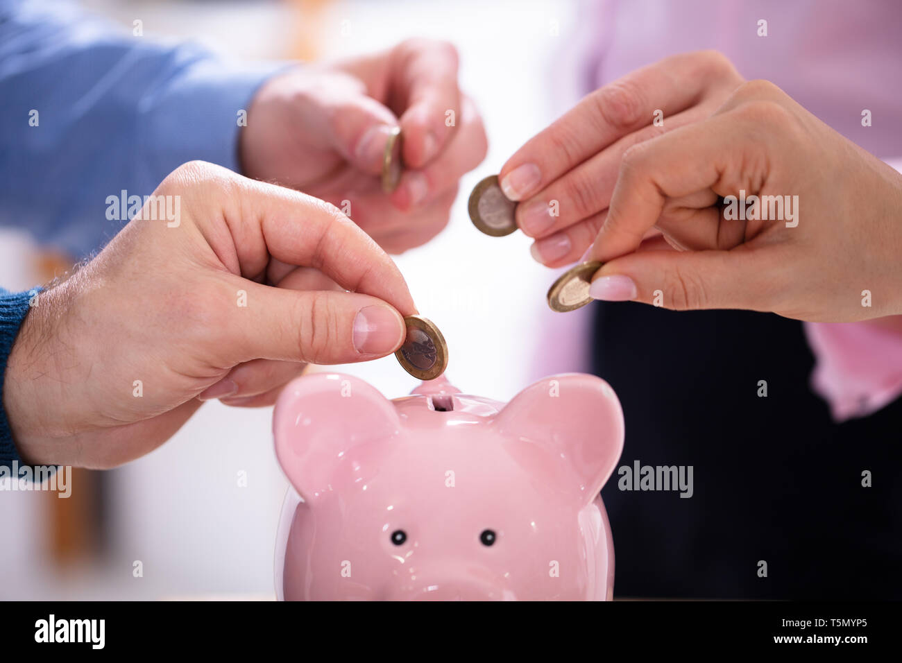 Gli imprenditori di mano inserire monete in rosa Piggybank in Office Foto Stock