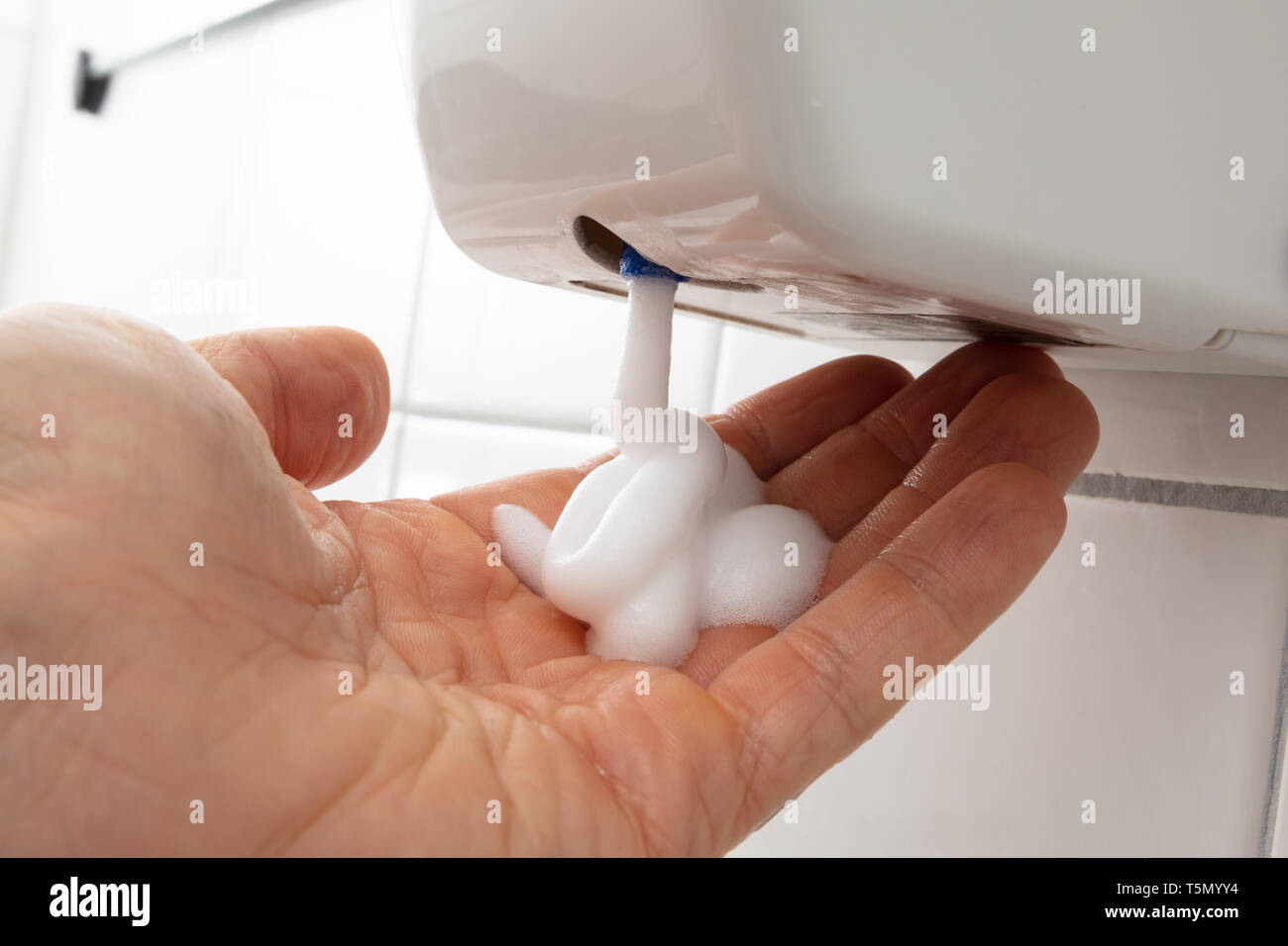 Close-up di persona la mano con dosatore per sapone liquido sulla parete piastrellata Foto Stock