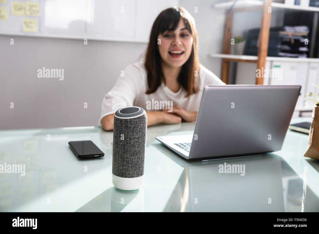 Sorridente giovane donna utilizzando Assistente vocale in Office Foto Stock