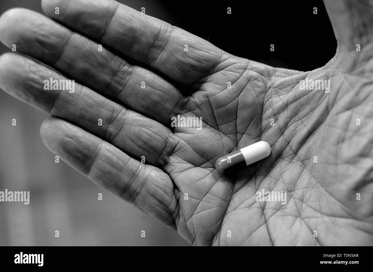 Un vecchio uomo detiene una pillola nel palmo della mano Foto Stock