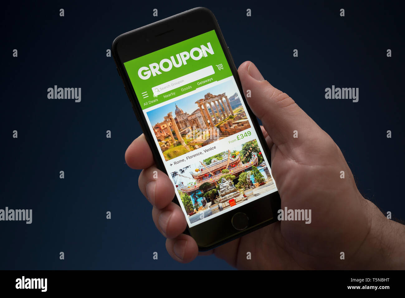 Un uomo guarda al suo iPhone che visualizza il logo Groupon (solo uso editoriale). Foto Stock