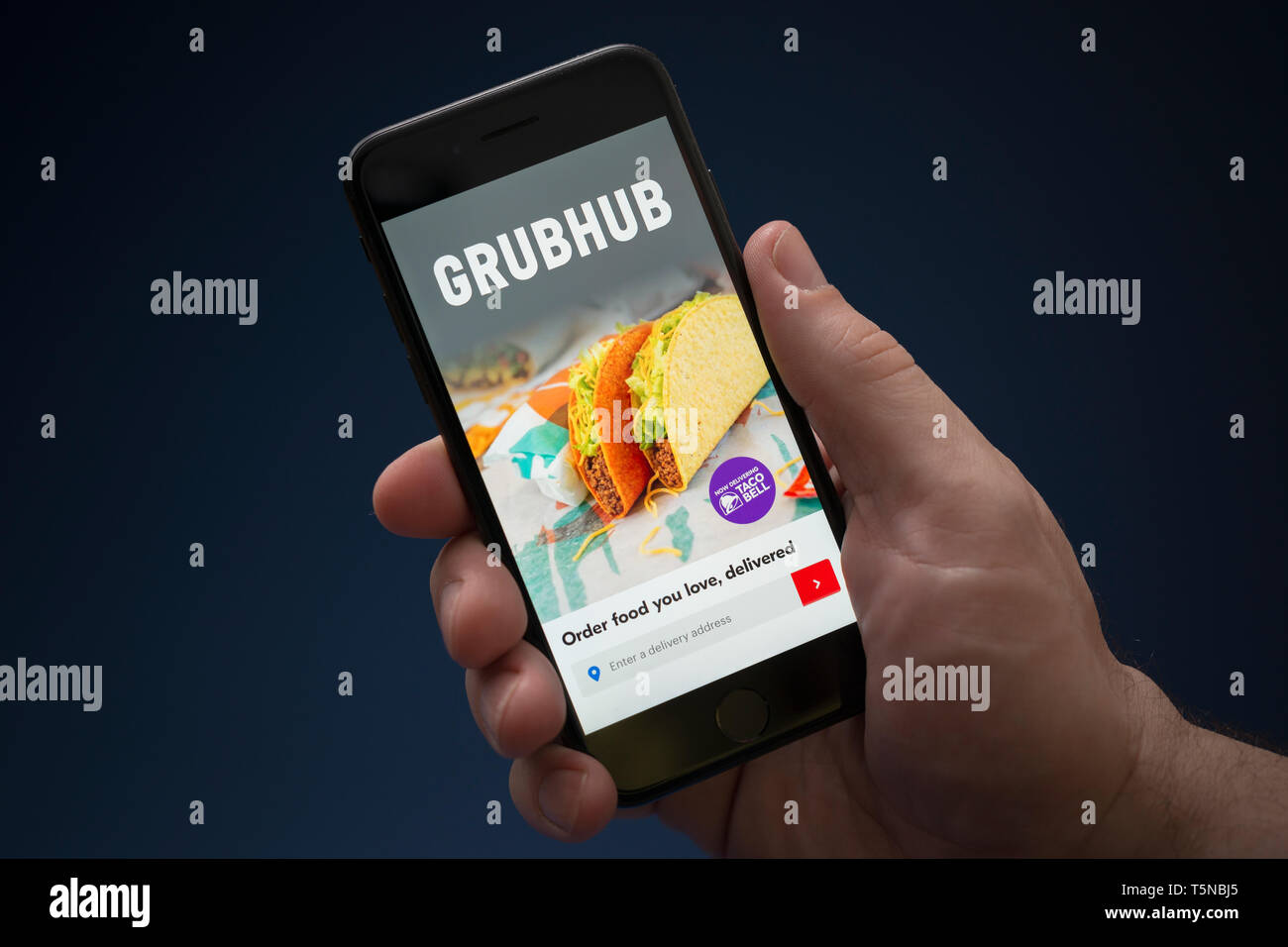 Un uomo guarda al suo iPhone che visualizza il logo Grubhub (solo uso editoriale). Foto Stock