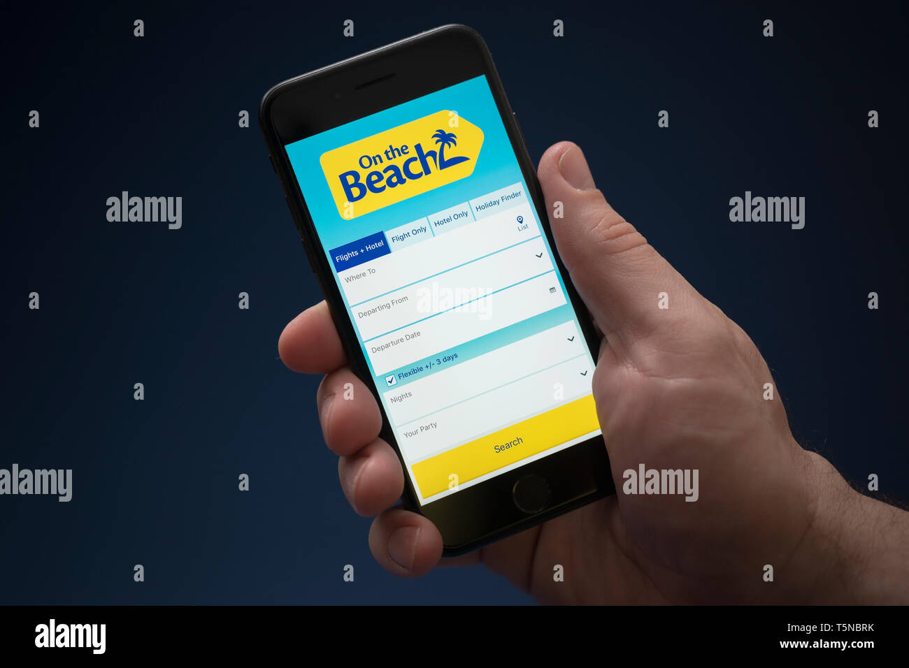 Un uomo guarda al suo iPhone che visualizza il sulla spiaggia logo (solo uso editoriale). Foto Stock