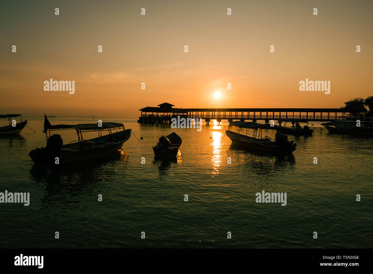Incredibile tramonto in una spiaggia tropicale con un molo e alcune barche in mare Foto Stock
