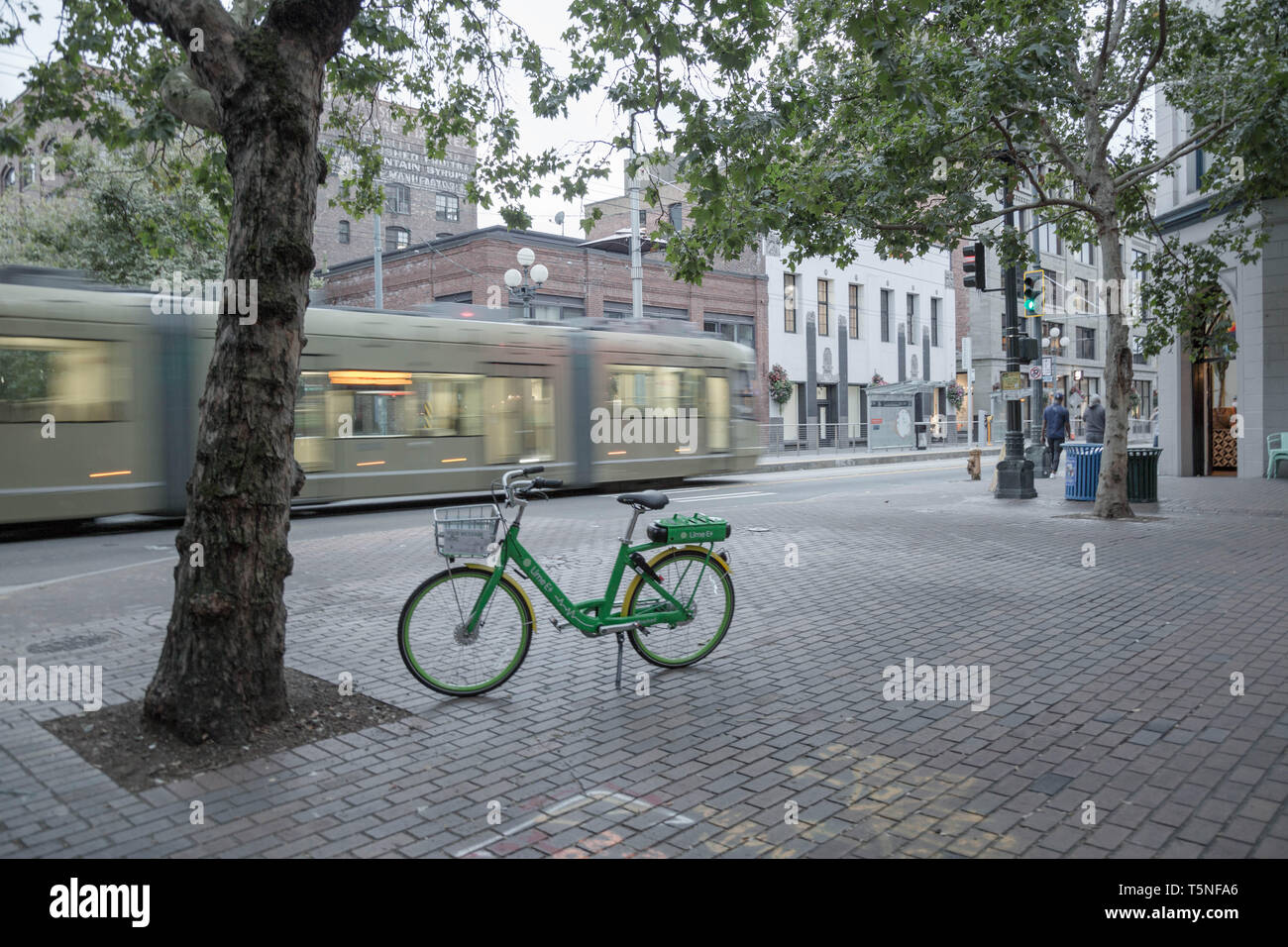 Seattle Pioneer Square, una linea ferroviaria leggera passa attraverso il pavimento di mattoni vicino a un pubblico Parcheggio Noleggio biciclette verniciati in città la firma di colore. Foto Stock