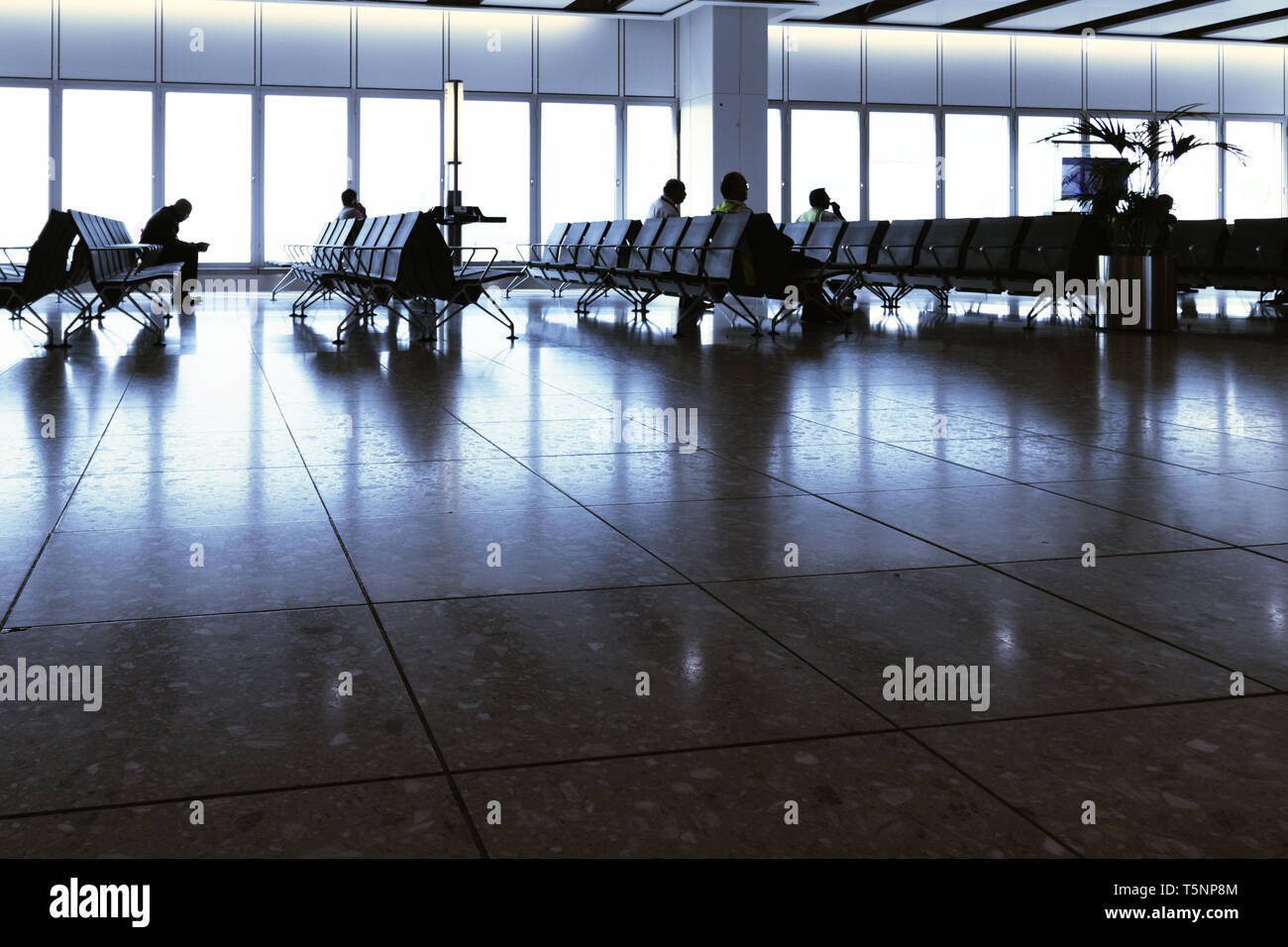 Il terminale 4,l'aeroporto di Heathrow di Londra, Regno Unito il 22 aprile 2019. Due uomini utilizzando gli smart phone sono seduti a un cancello in aeroporto in attesa a bordo di un volo Foto Stock