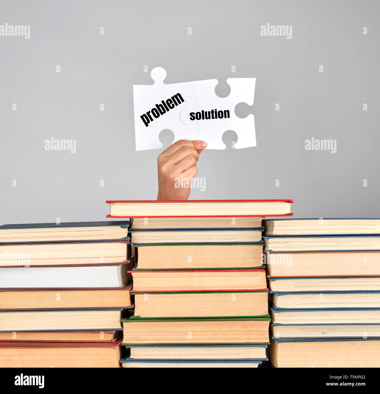 Mani femminili azienda grande puzzle bianco su una pila di libri e sfondo grigio, problem solving concept Foto Stock