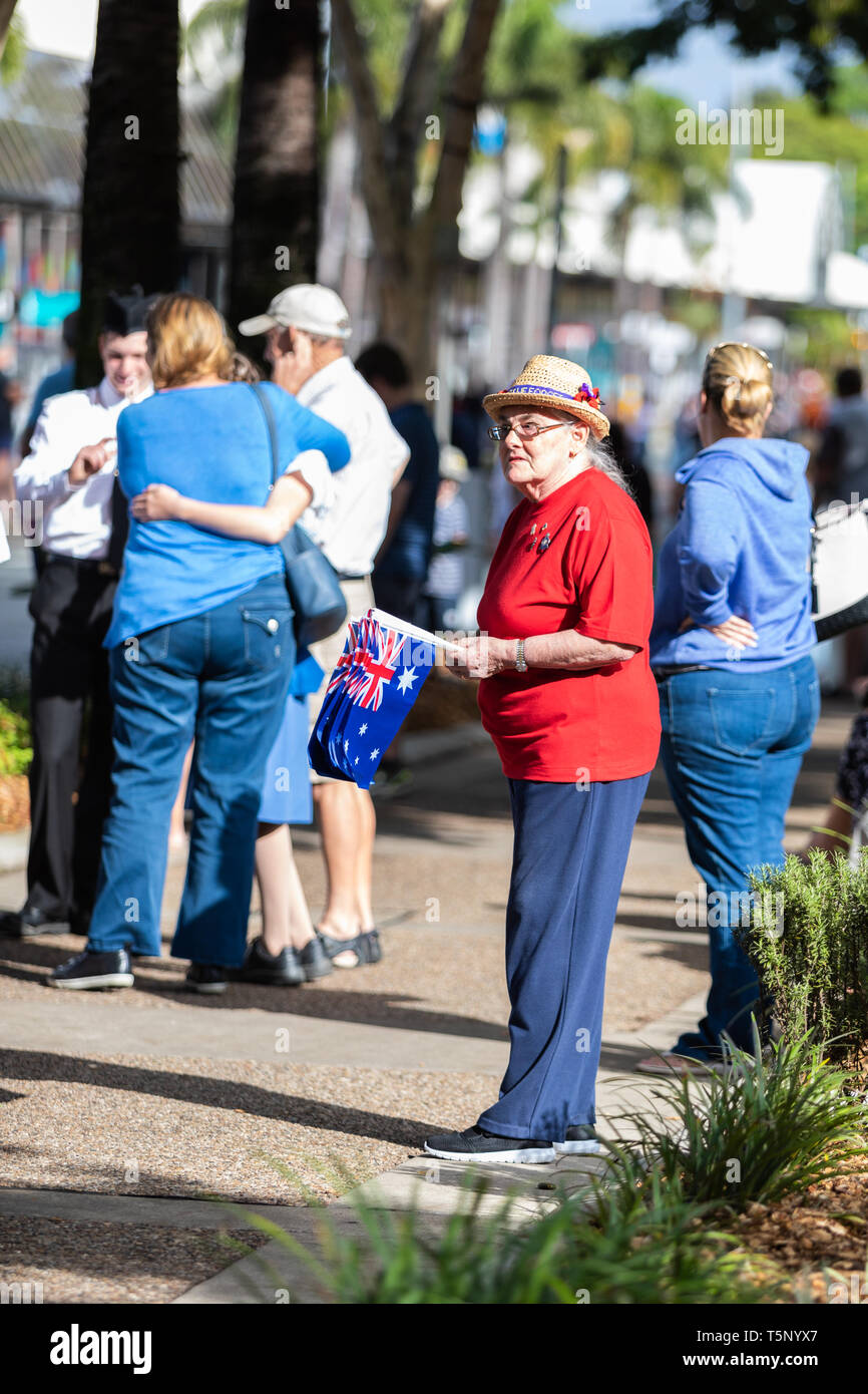 Una gentile signora anziana distribuendo piccole bandiere Australiano per le persone che frequentano l'Anzac Day marzo, indossando i colori luminosi e un cappello con il papavero Foto Stock