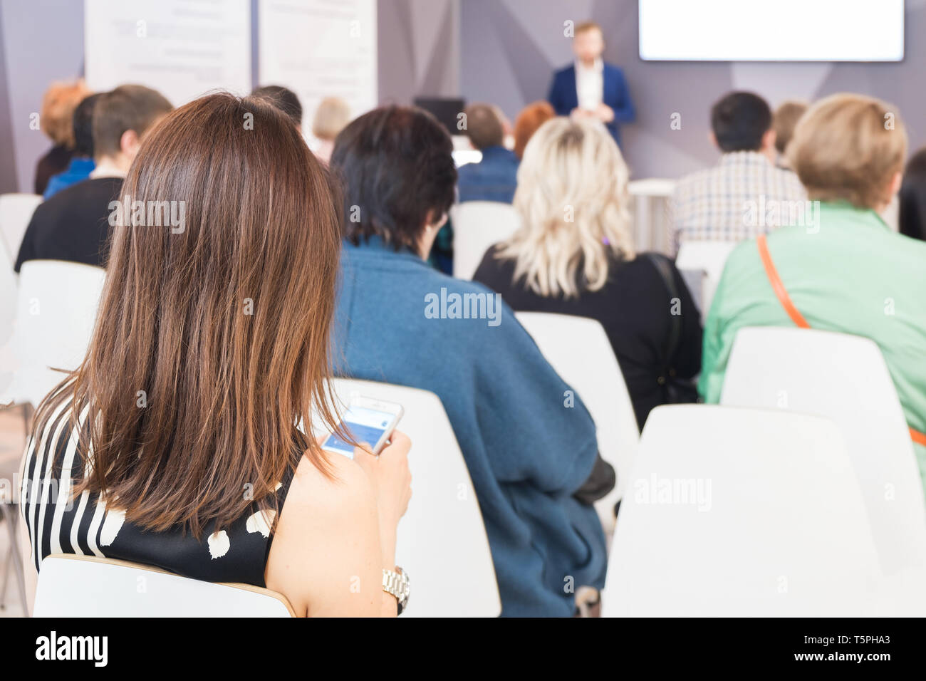 Business donna con uno smartphone in mano e persone in ascolto sulla conferenza. L'immagine orizzontale Foto Stock