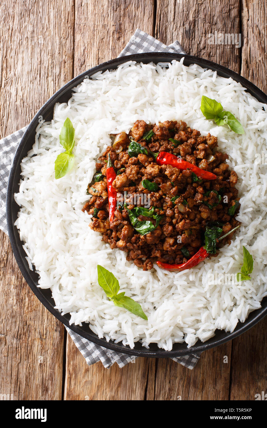 Pollo di basilico (Gai Pad Krapow) - il pollo, Aglio Scalogno, dolce la salsa di soia, il basilico e il riso close-up su una piastra sul tavolo. Verticale in alto vista da un Foto Stock