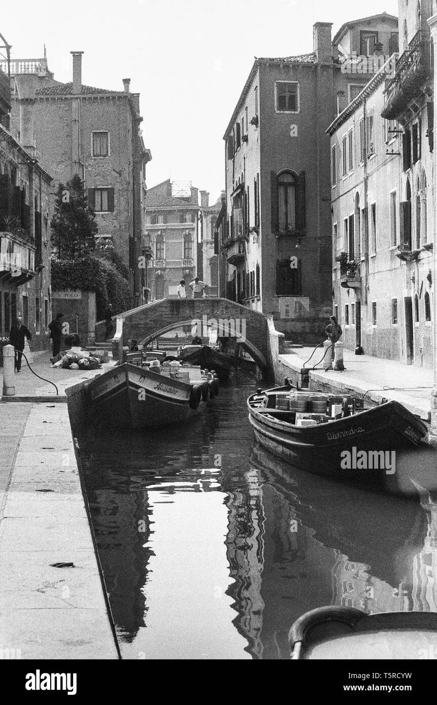 Venezia - Italia - 1980 - foto in bianco e nero: caratteristica venezia canal, stretta tra le case con un piccolo ponte in background e due barche in primo piano Foto Stock